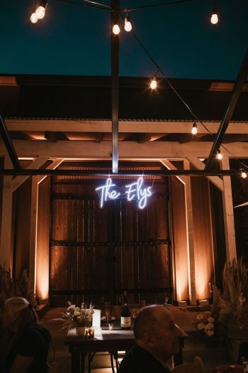 An evening event setting with "the elys" neon sign above a well-lit seating area.