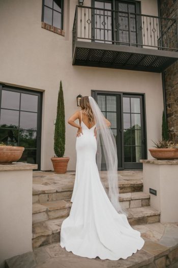 Bride in a white gown standing outside a building with a balcony.