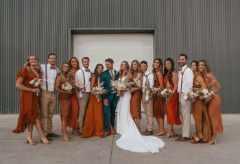 A wedding party posing for a photo with the bride and groom centered, flanked by bridesmaids and groomsmen in coordinating outfits.