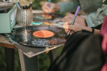 Person writing with a purple marker on a vinyl record that is set on a table outdoors.