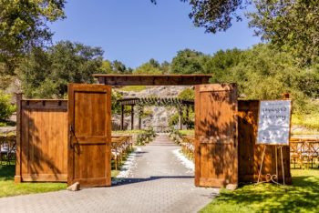 Outdoor wedding venue with wooden gates open to a pathway leading to a ceremony arch.