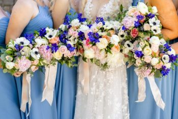 Bride and bridesmaids holding bouquets with blue and white flowers.