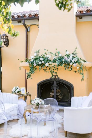 An elegantly decorated outdoor seating area with floral arrangements above a fireplace.