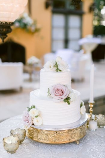 Elegant white wedding cake adorned with fresh flowers on a golden stand.