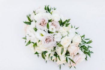 A bouquet of pale pink and white flowers with green foliage on a white background.