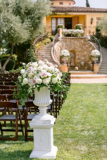 Elegant outdoor wedding venue setup with floral arrangement and seating facing a staircase.
