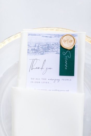 Elegant wedding thank you card with green accent, displayed on a white napkin and gold-rimmed plate.