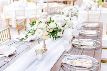 Elegant outdoor wedding reception table setting with white floral centerpieces.