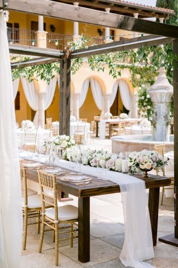 An elegantly set outdoor wedding reception table with floral centerpieces.