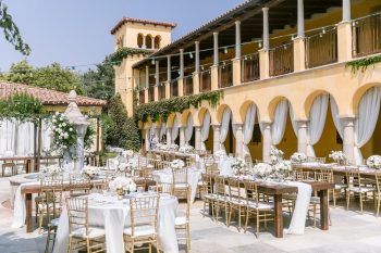 Elegant outdoor wedding setup with white floral arrangements in front of a mediterranean-style building.