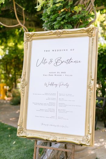 An ornate gold frame displaying a wedding sign with names and event details.