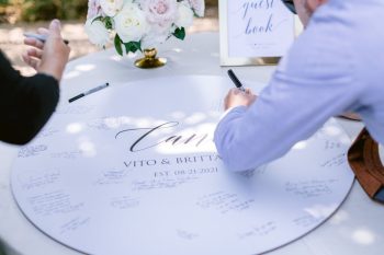Guest signing a white wedding guestbook table with names and date of the event inscribed in the center.
