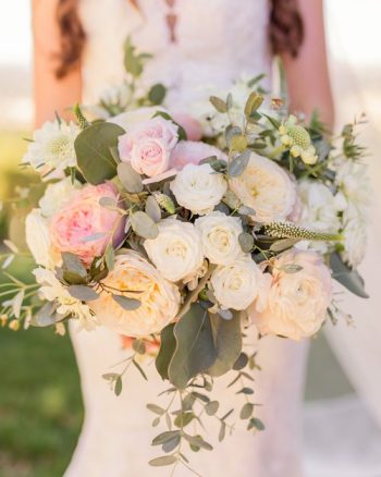 Bride holding a bouquet of pink and white flowers with green foliage.