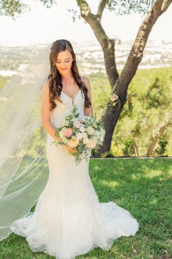 Bride holding a bouquet while smiling outdoors.