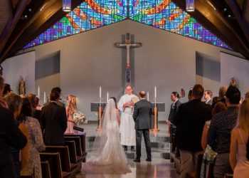 Wedding ceremony in progress at a church with a stained glass background.