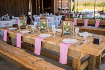 Rustic wedding reception table setting with pink accents and decorative lantern centerpieces.