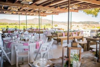 Outdoor dining setup with elegantly arranged tables under a covered patio with a scenic backdrop.