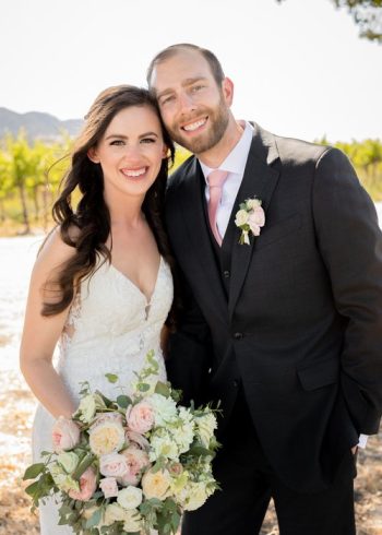 A smiling couple in formal wedding attire, posing for a photograph outdoors.
