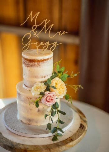 A two-tiered wedding cake with floral decoration and "mr & mrs gregg" topper.