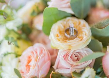 A diamond engagement ring resting on a delicate yellow rose amidst a floral bouquet.