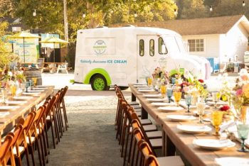 An ice cream truck parked near a decorated outdoor dining area with arranged tables and chairs.