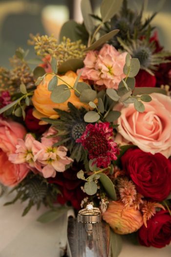 Elegant floral arrangement featuring roses and greenery with a pair of wedding rings nestled on a petal.