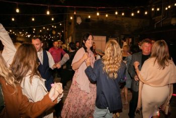 Group of people enjoying an outdoor evening party with string lights overhead.