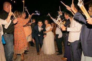 A newlywed couple walking through a sparkler send-off as guests cheer them on.