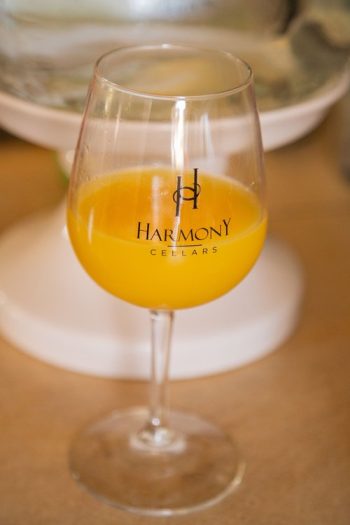 Glass of orange juice on a table with the logo "harmony cellars" printed on it.