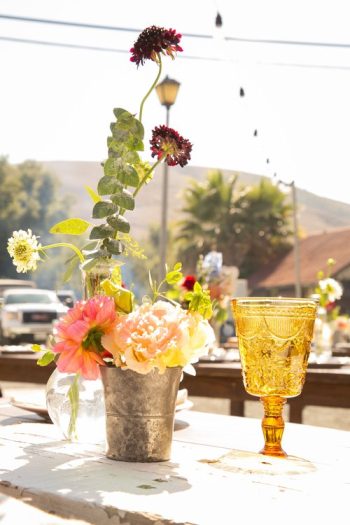 Al fresco table setting with a rustic flower arrangement and an amber-colored glass in the sunshine.