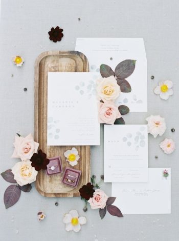 Elegant wedding invitation suite displayed with floral accents and ring boxes on a wooden tray.