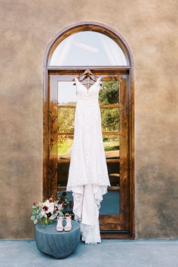 A wedding dress hanging on a wooden door, with bridal shoes and a bouquet arranged beside it.