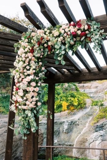 Floral arrangement decorating a wooden pergola with a rockery background.