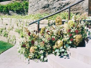 Stone steps adorned with greenery and flowers next to a metal handrail.