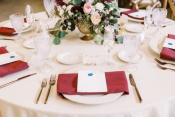 Elegant dining table setting with floral centerpiece and burgundy napkins.