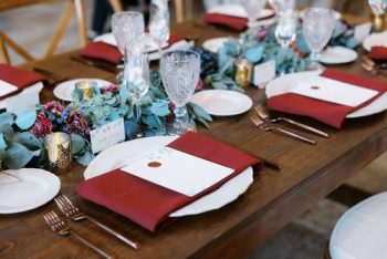 Elegant dining table setting with maroon napkins and blue floral centerpiece.