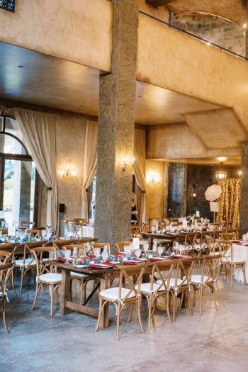 Elegant dining setup with wooden tables and chairs in a room with draped curtains and warm lighting.