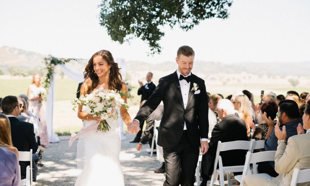 Bride and groom walking hand in hand down the aisle after their wedding ceremony, with guests looking on and applauding.