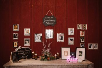 A memorial table at a wedding with photos, candles, and a sign reading "in loving memory of those who are forever present in our hearts.