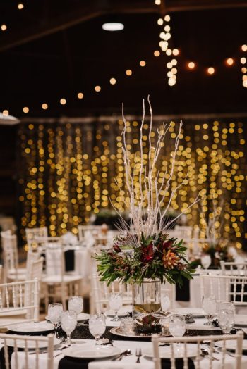 Elegant banquet table setting with a tall floral centerpiece and a backdrop of twinkling lights.