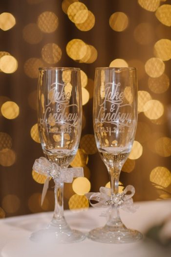 Two personalized champagne glasses with names and a date, set against a bokeh light background, suggesting a celebratory event.