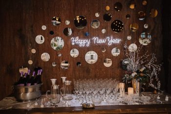 A festive new year's celebration display featuring a neon 'happy new year' sign, champagne, glasses, and decorative backdrop.
