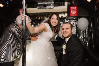 Bride and groom smiling inside a decorated bus with a guest entering.