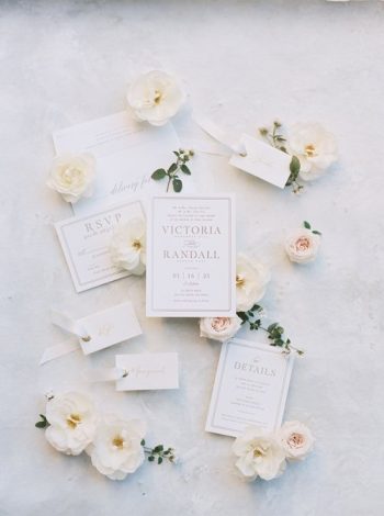 Elegant wedding invitation suite surrounded by delicate white flowers on a light background.