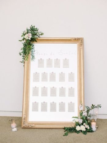 Elegant wedding seating chart framed in gold with floral decoration.