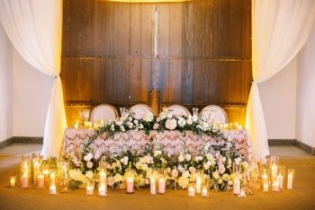 Elegant wedding head table adorned with floral arrangements and surrounded by candles.