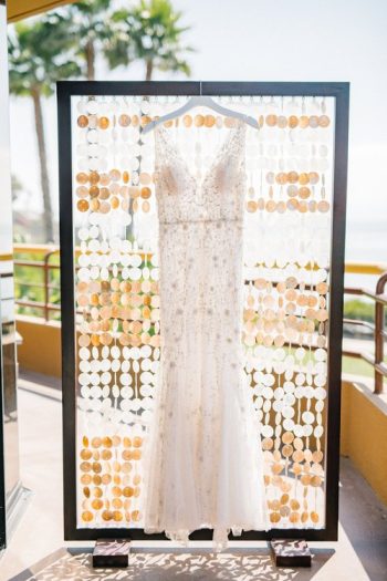 A wedding dress hanging on a decorative stand with a patterned backdrop.
