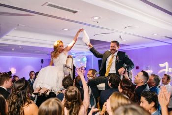 Bride and groom being lifted on chairs during a wedding reception celebration.