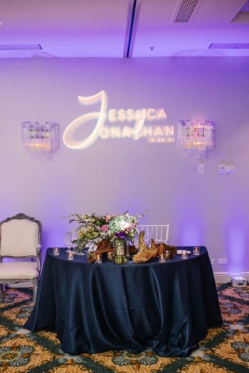 Elegant sweetheart table set for a wedding reception with the names 'jessica & jonathan' illuminated on the wall.