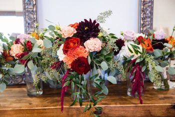 Floral arrangement on a wooden table featuring a variety of colorful flowers and greenery.
